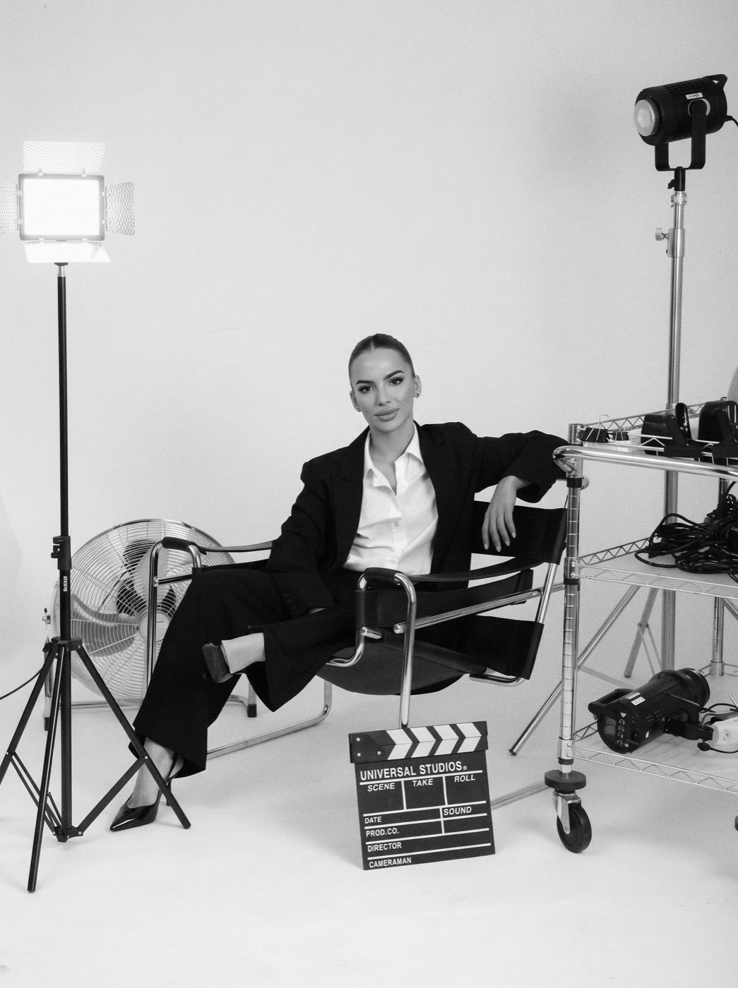 Black-and-white studio portrait of Ines seated in a director's chair, lights and clapperboard around her.